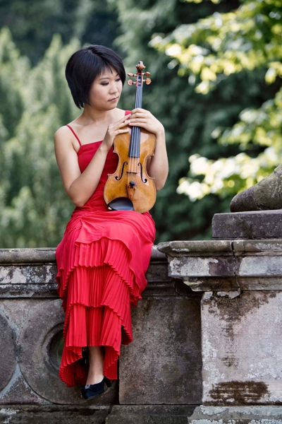 Tianwa Yang im roten Kleid, sitzt auf einer Mauer.
